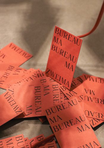 Viele Letterpress Visitenkarten in Hochformat in orange zeigen das Branding (Corporate Design) der Freelance Grafikdesign Designagentur Bureau Zweima. Eine Visitenkarte ist an ein Kabel angelehnt